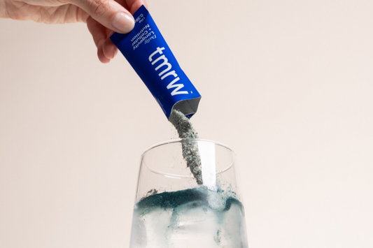 Tmrw powder being poured from a blue sachet into a glass of water.